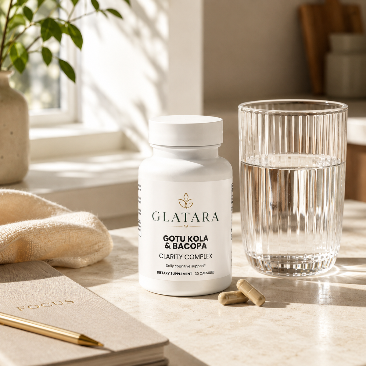 A white bottle of Glatara Gotu Kola & Bacopa Clarity Complex dietary supplement stands on a light marble surface beside a glass of water, with two capsules in front and a notebook with a gold pen nearby in a softly lit interior setting.
